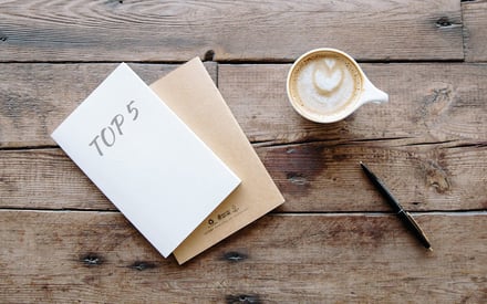 Folder with "top 5" written on the front and a cup of coffee and a pen on a table