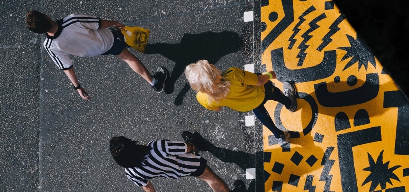 Three people walking on yellow & black colored pavement