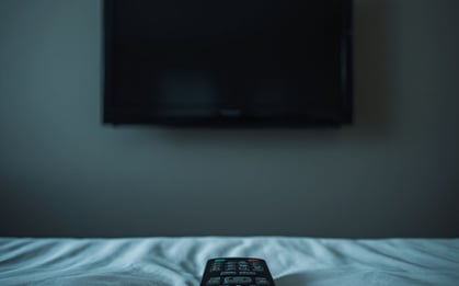 Photorealistic image of a hotel room wall-mounted TV with a clunky on-screen menu, a remote control resting on the bed in the foreground