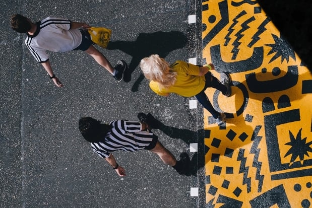 Three people walking on yellow & black colored pavement