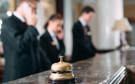 Hotelrezeption, wobei die Hotelglocke im Fokus steht und das Personal im Hintergrund unscharf ist