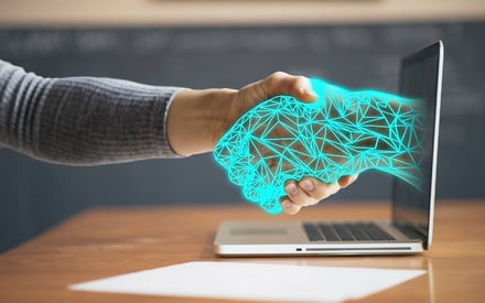 Human hand shaking an AI hand coming out of a laptop