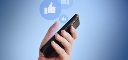 A hand holding a mobile phone agains a blue background with review pop up thumbs up images coming out of the device