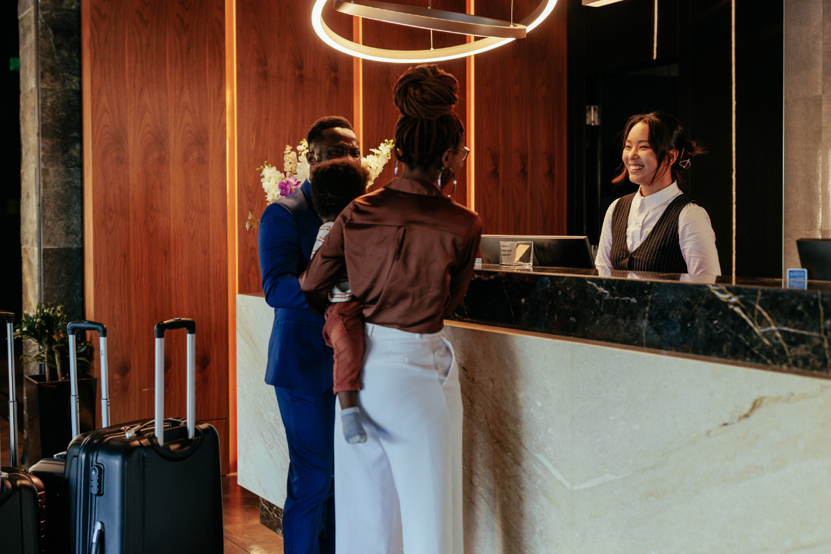 Modernes Hotelzimmer, dargestellt als drei klar voneinander getrennte Bereiche, durch Wände separiert: links eine Familie mit Kindern beim Ankommen, in der Mitte ein Paar, das gemeinsam entspannt auf dem Bett sitzt, rechts ein Geschäftsreisender, der am Schreibtisch arbeitet.